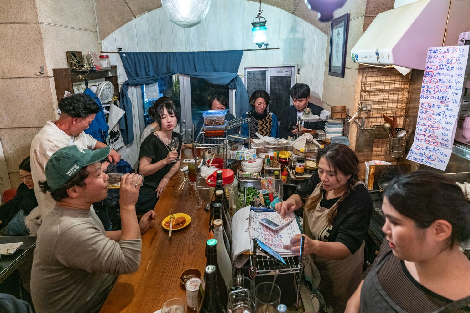 Crowded bar scene with patrons and bartenders interacting across a busy counter in a cozy establishment.