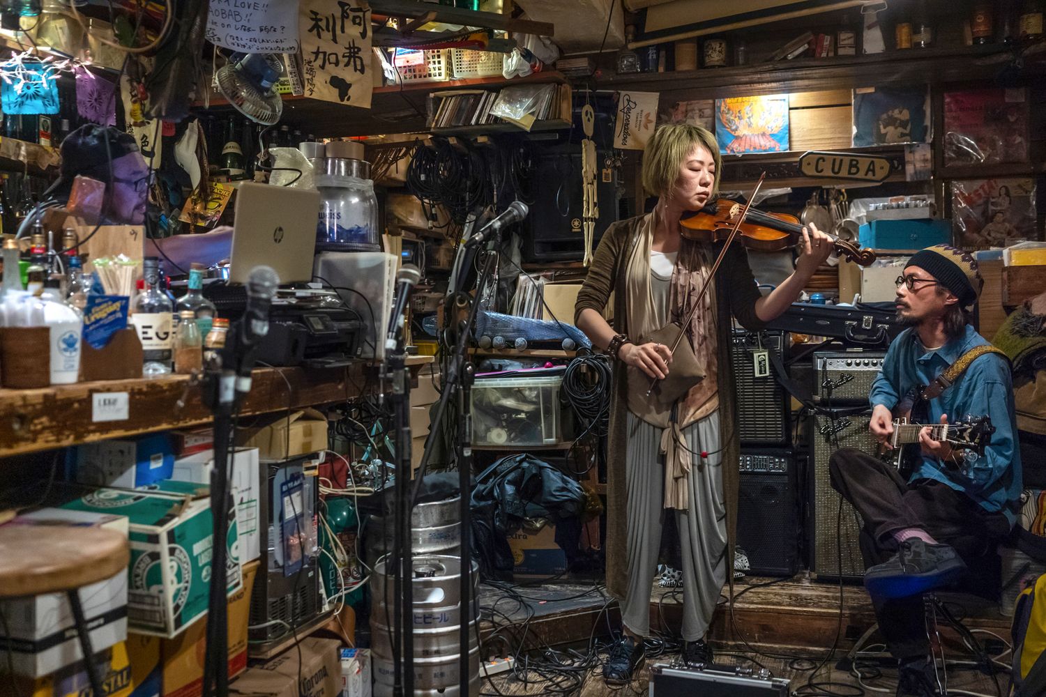 Musicians performing with violin and guitar in a cluttered vintage store setting.