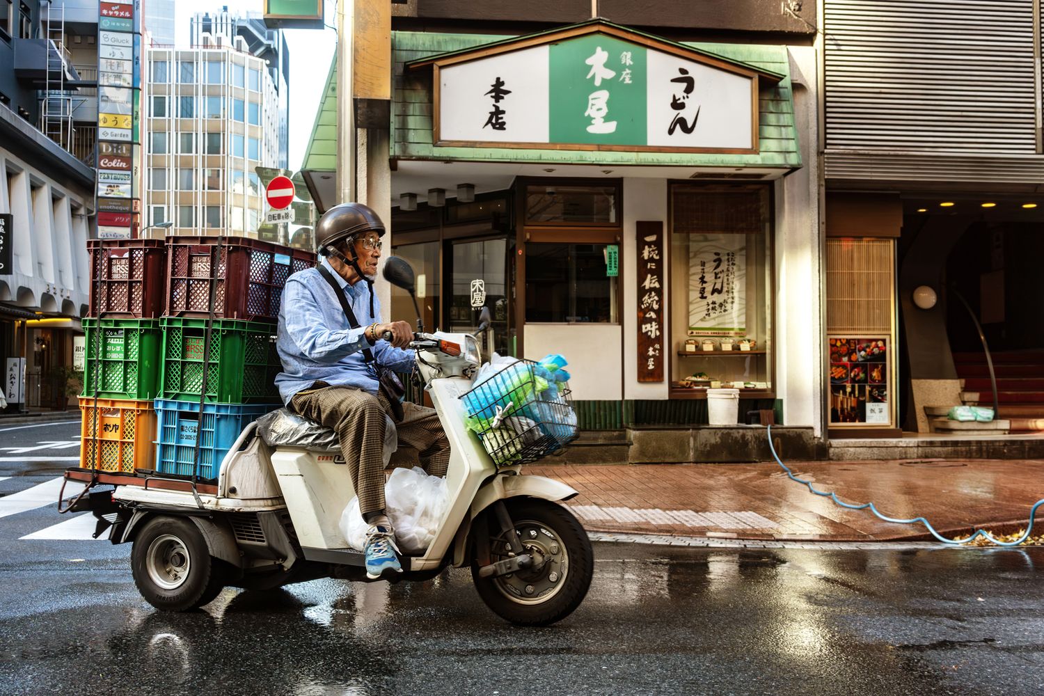 Delivery scooter parked outside traditional Japanese shops on rainy street.