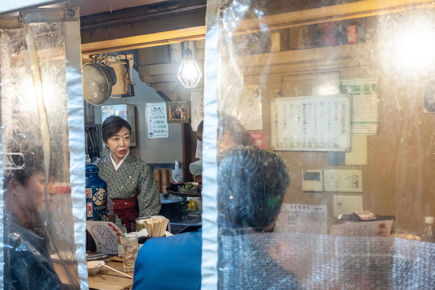 Steam rises inside a traditional Japanese restaurant kitchen viewed through window.