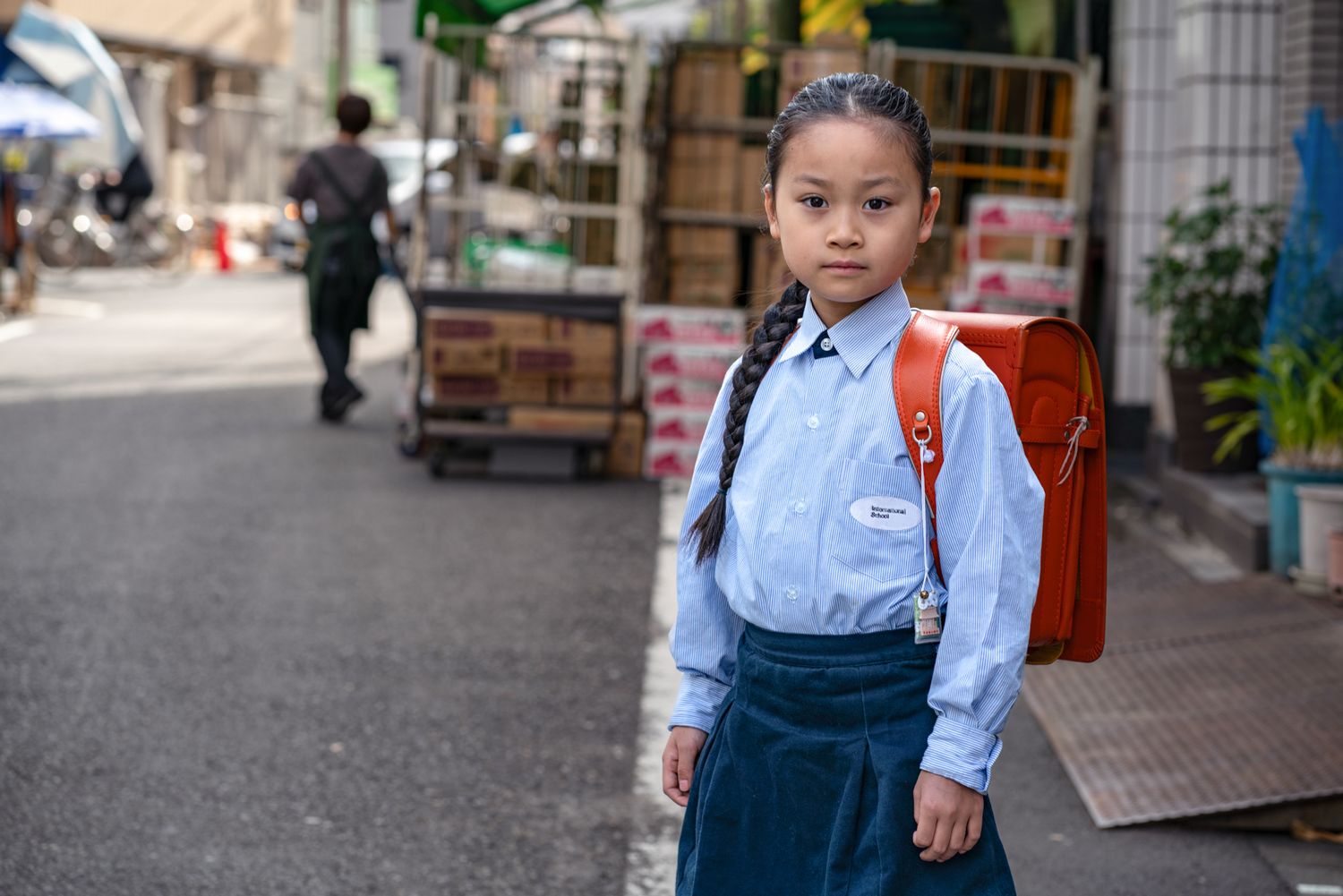 Student in uniform with red backpack standing on a quiet Japanese street.