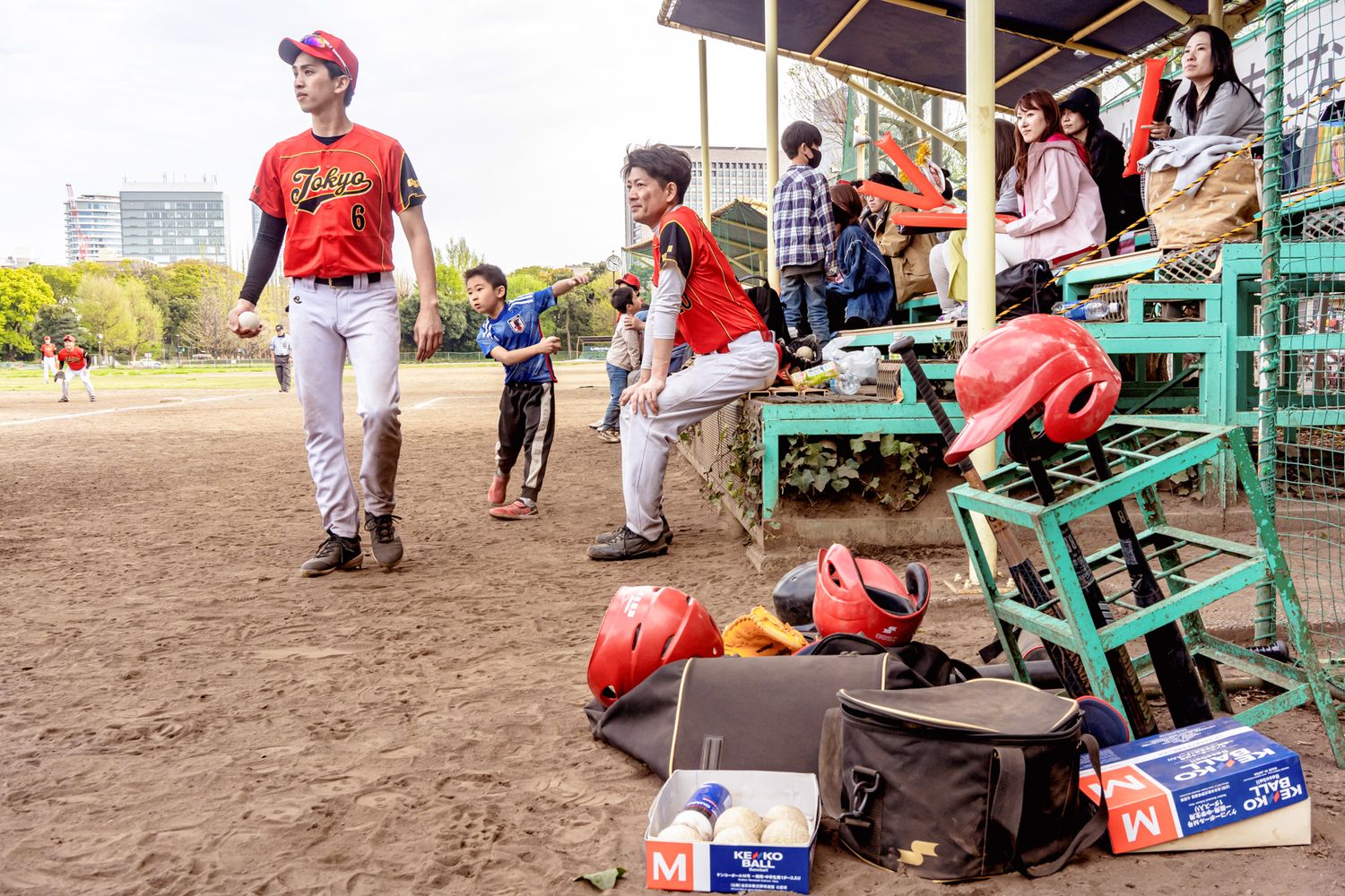 Baseball players in red uniforms gather around dugout benches on a dirt field.
