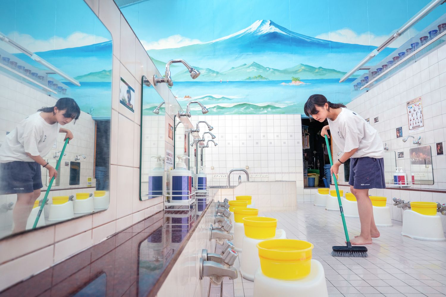 Public bathhouse interior with painted Mount Fuji mural and yellow washing buckets.