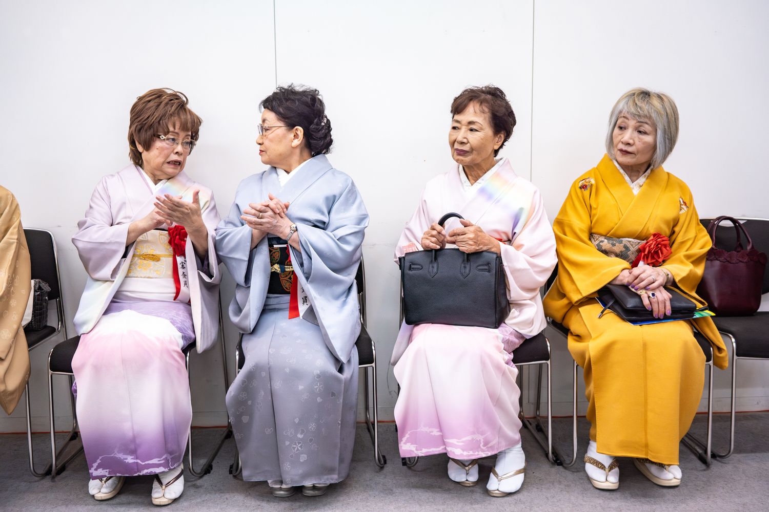 Four women in colorful kimonos sit together on chairs having an animated conversation.