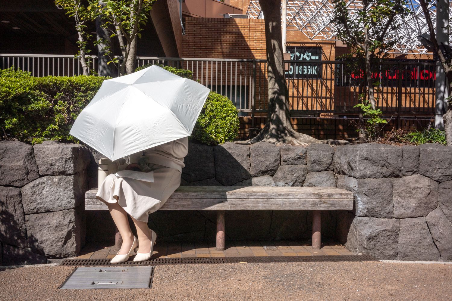 Person with white umbrella sitting on stone bench in urban setting.