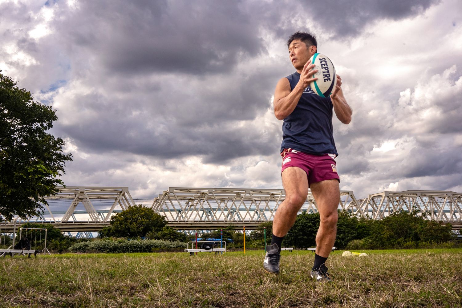 Rugby player jumping with ball against dramatic cloudy sky and stadium backdrop.