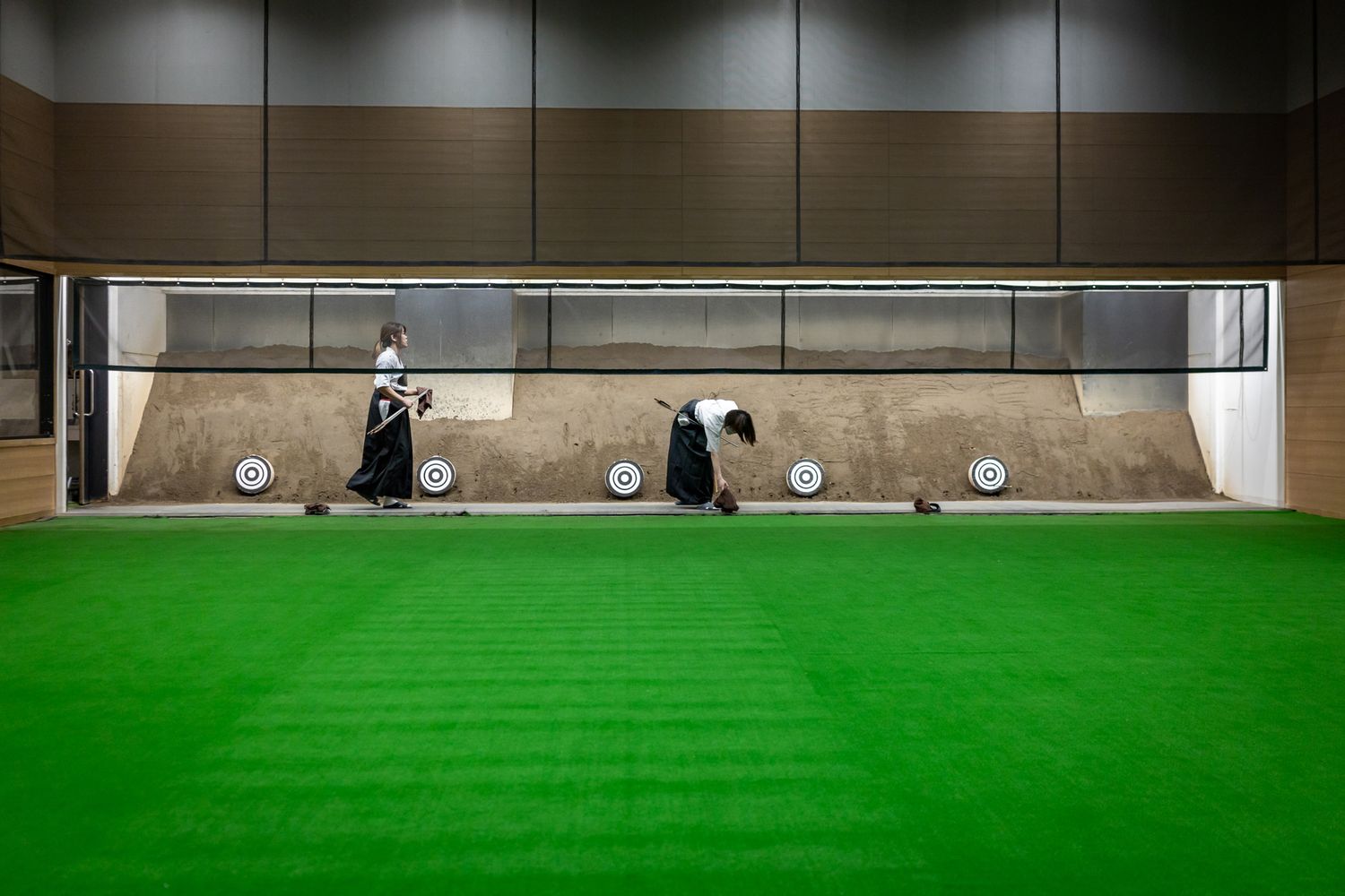 Indoor golf practice facility with green turf and practice bays.