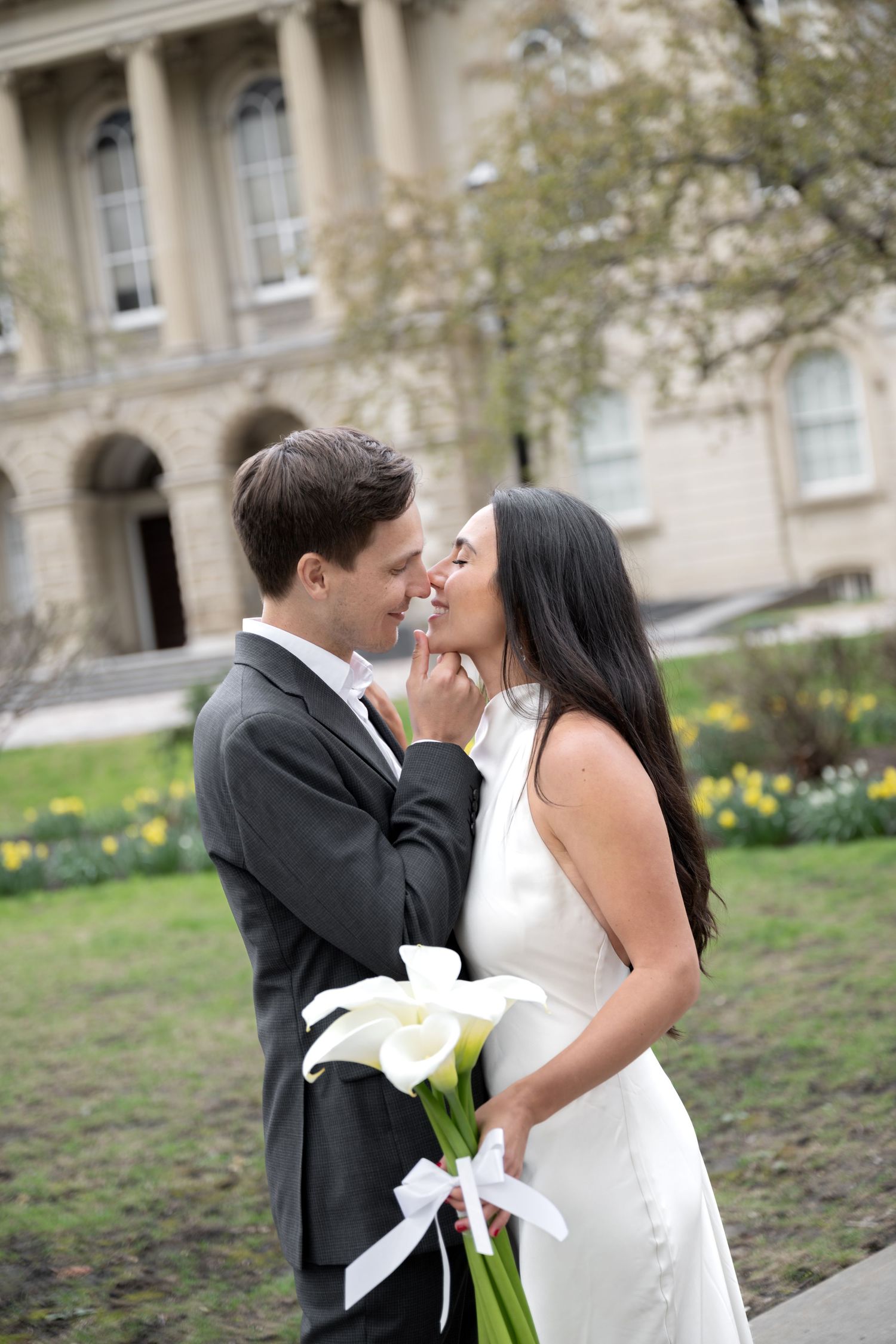 Romantic couple embracing with calla lily bouquet in front of classic architecture building.