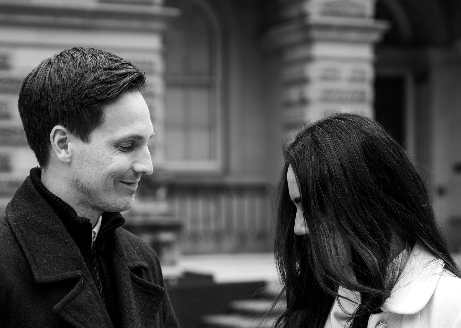 A candid black and white photograph of a couple sharing a tender moment outdoors.