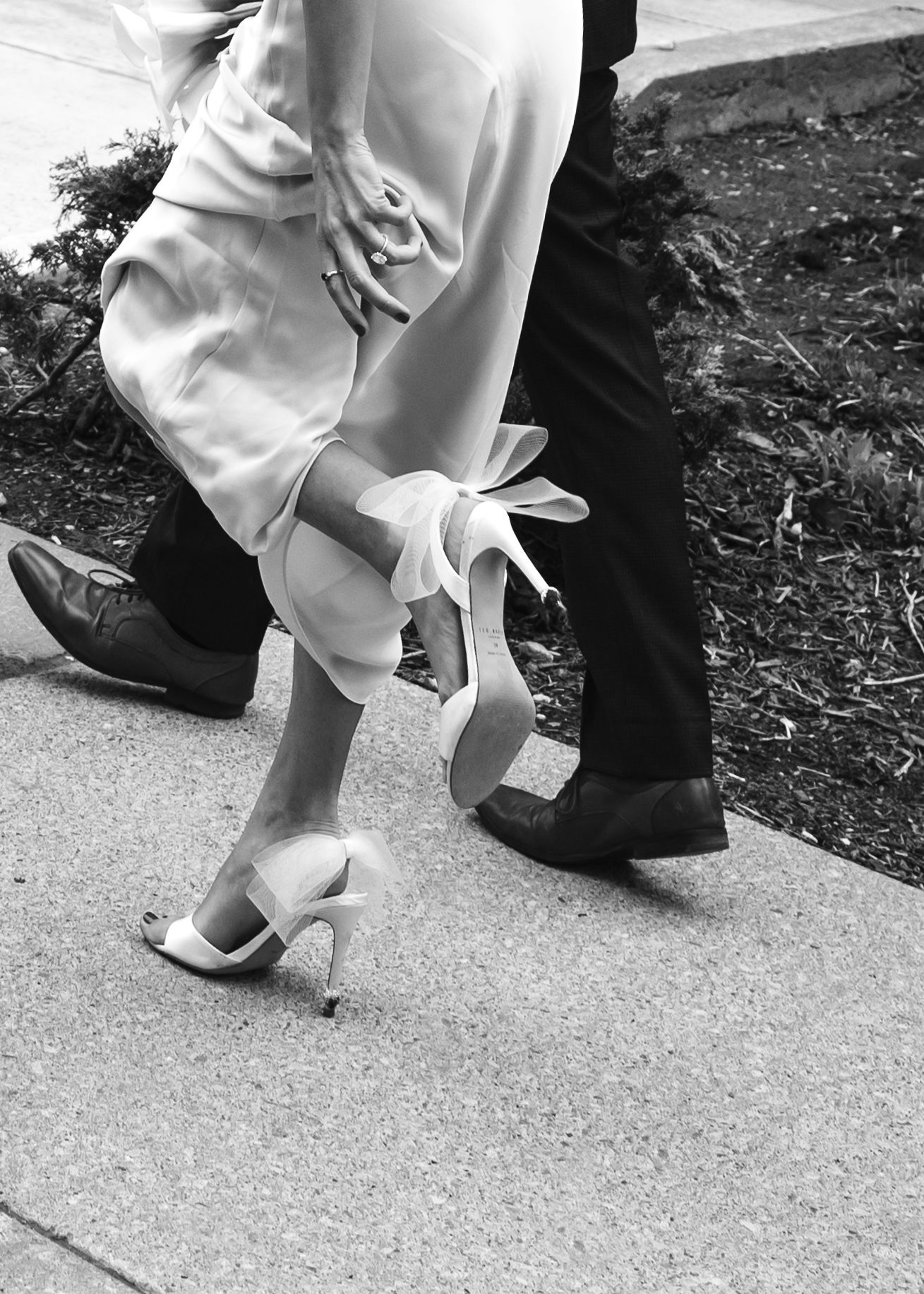 Black and white photograph showing elegant dress shoes and heels on pavement in a candid dance-like pose.