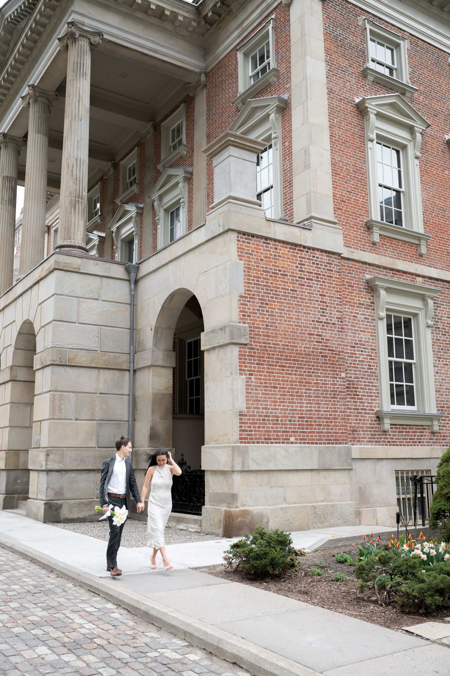 A elegant couple stands outside a historic brick building with classical columns and architectural details.