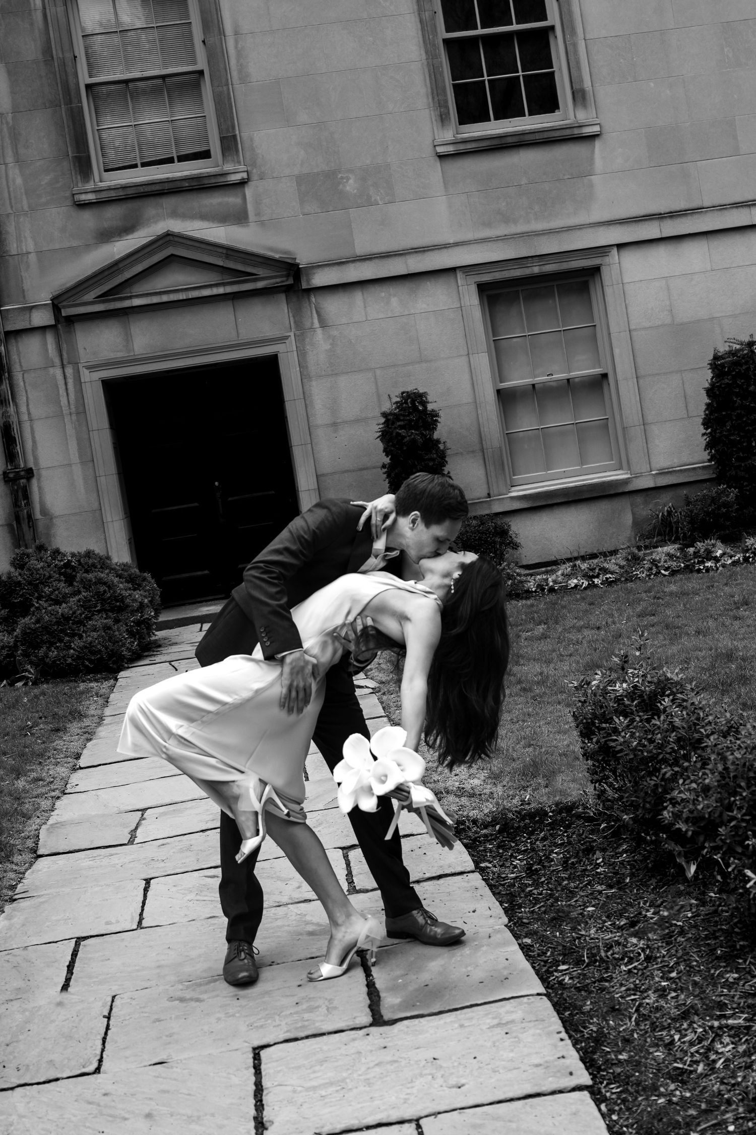 A romantic black and white photo of a couple performing a dramatic dip pose on a stone pathway.