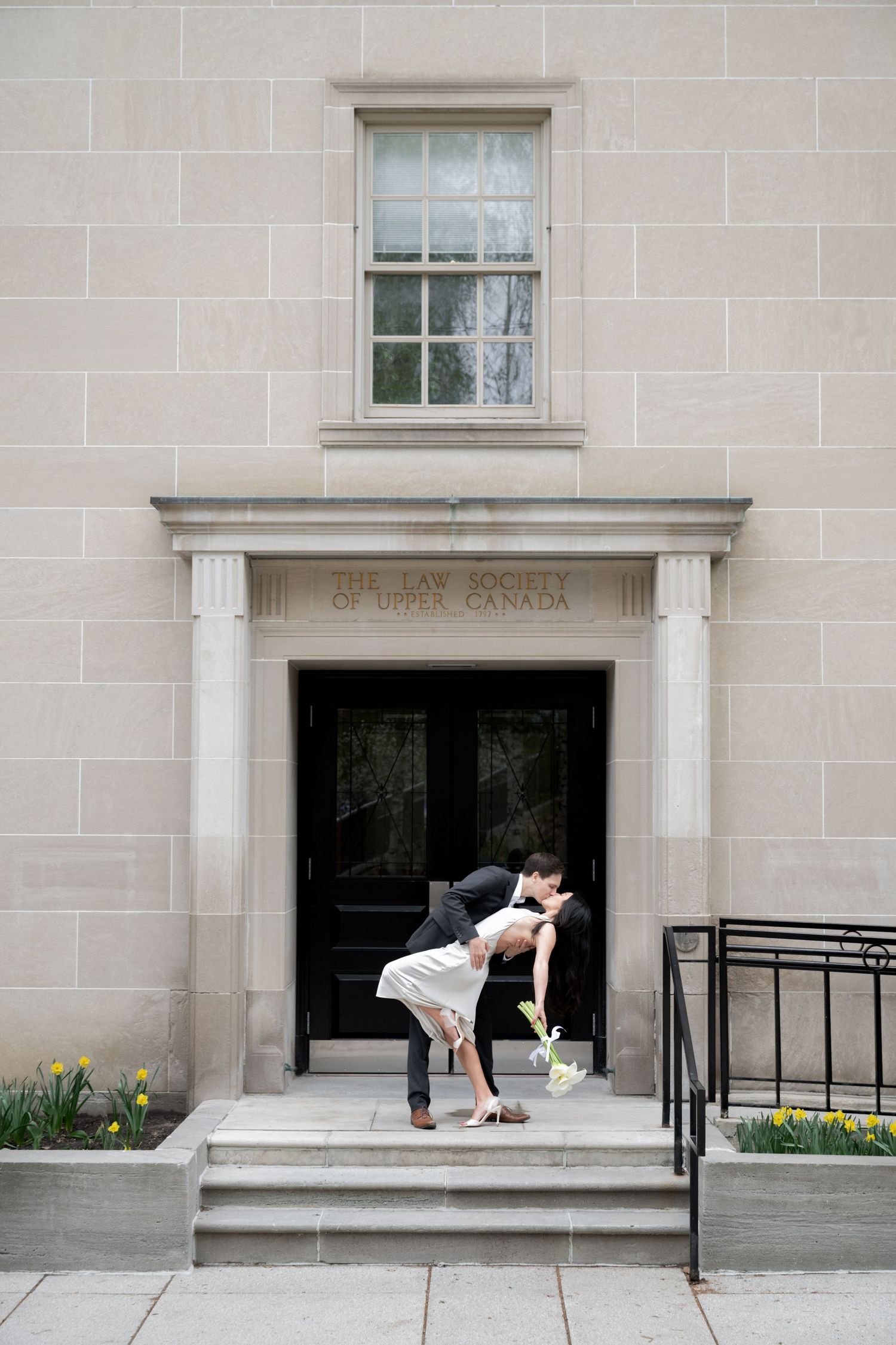 A lighthearted moment captured outside a stone building with 'Bank of Canada' text above dark double doors.