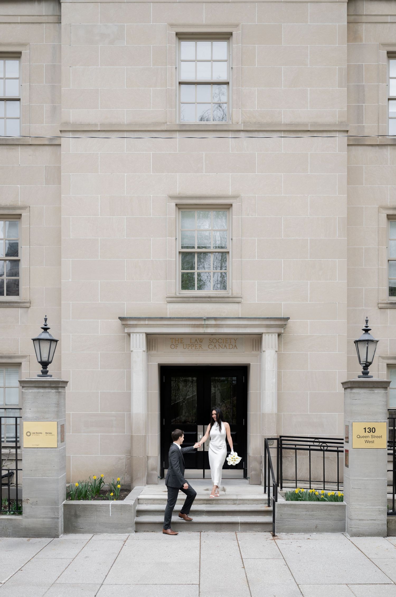 Two people approach the entrance of a classic stone building with lanterns and a light beige facade.