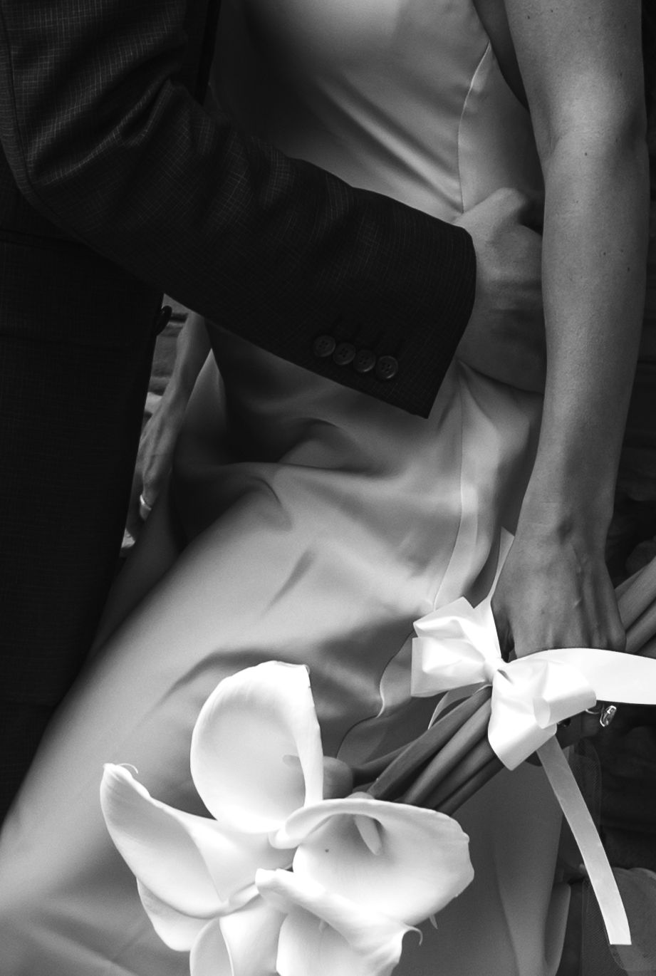 Black and white artistic photograph of a white calla lily flower against formal attire fabric.