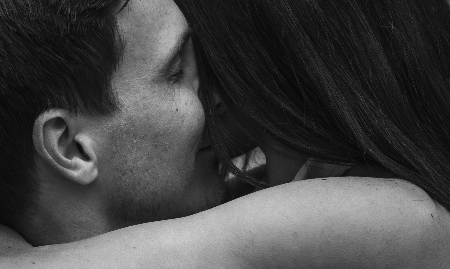 An intimate black and white portrait showing a tender kiss on the shoulder.