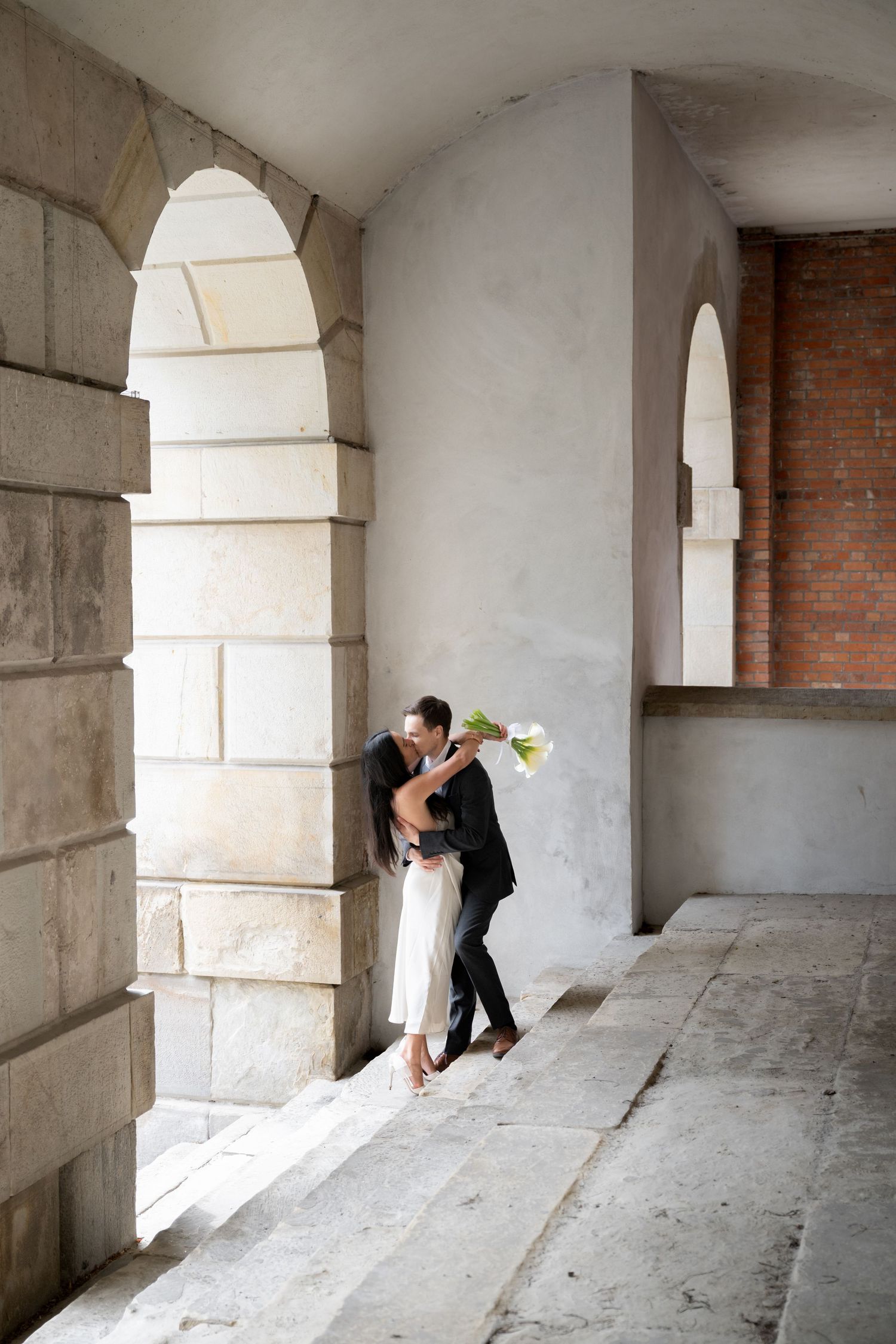 Romantic couple embracing under stone archway with natural light streaming in.