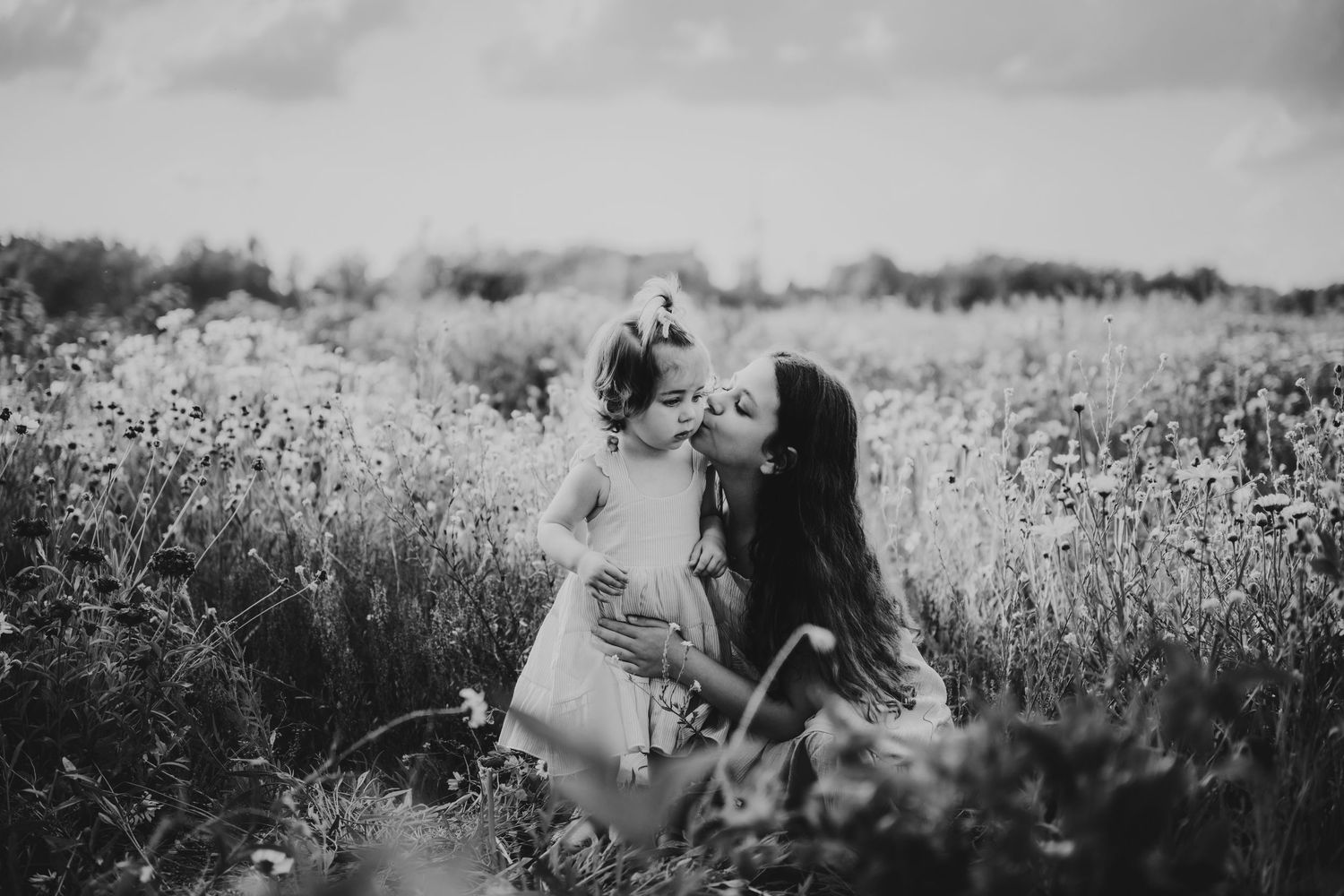 A black and white photograph shows someone lying in a meadow of tall wildflowers on a sunny day.