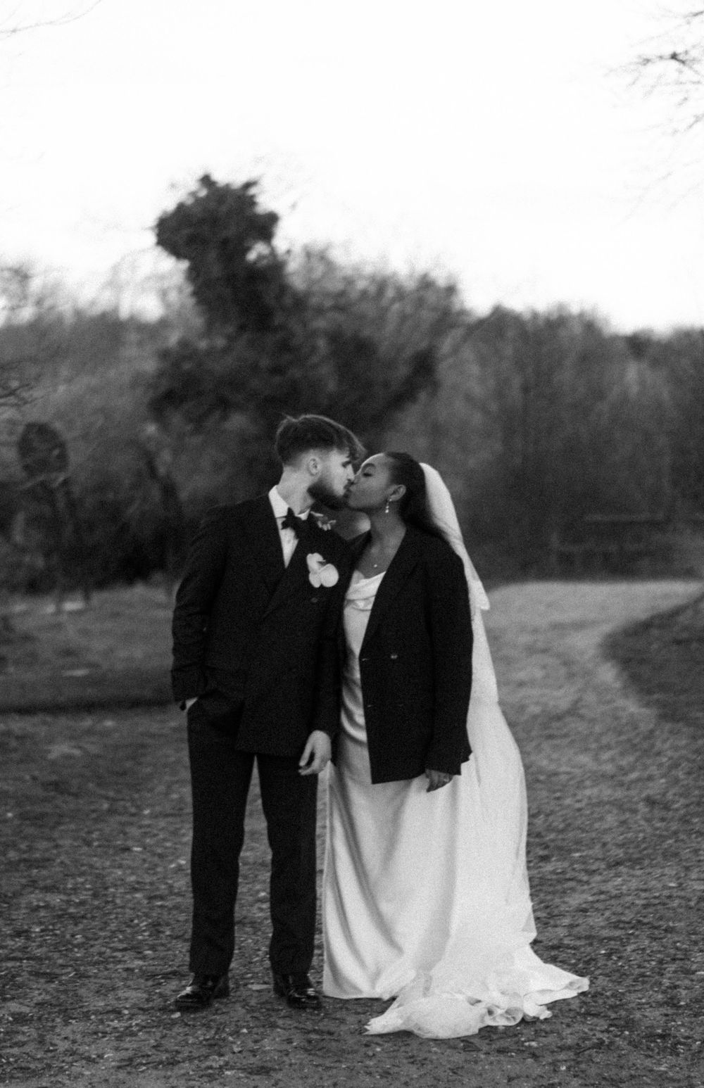 Portrait of Bride & Groom sharing a kiss, bride wearing a blaze over her wedding dress. Editorial wedding