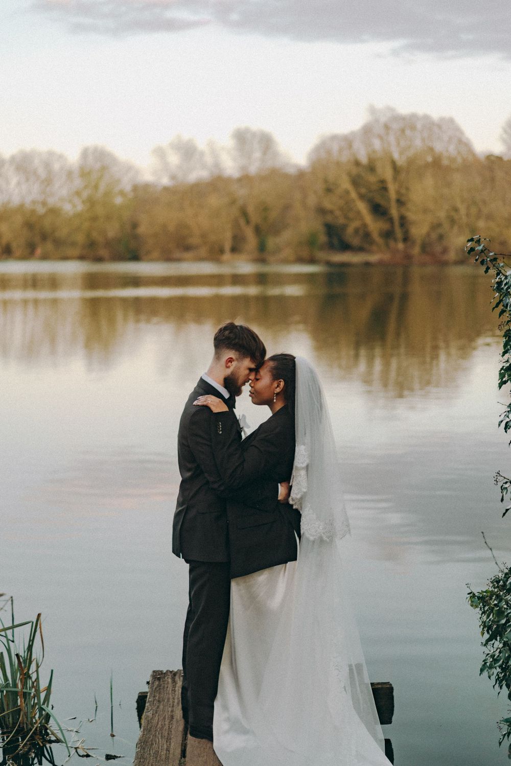 Medium photo of Bride groom in an embrace, foreheads adjoined to the backdrop of a lake. Documentary wedding