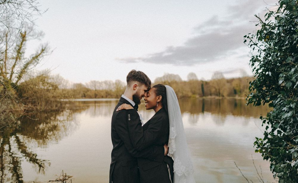 Bride groom in an embrace, foreheads adjoined to the backdrop of a lake. Documentary wedding