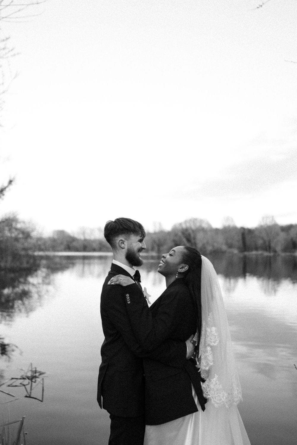 Bride groom in laughing whilst in an embrace, foreheads adjoined to the backdrop of a lake. Documentary wedding