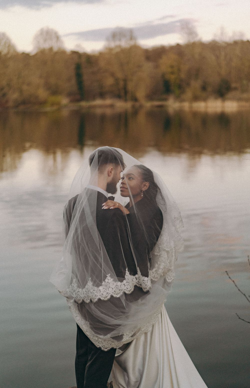 Bride groom in an embrace (under veil) to the backdrop of a lake. Documentary wedding