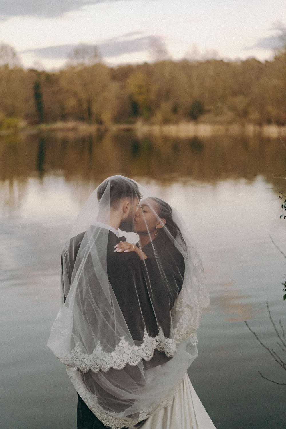 photo of bride groom sharing kiss (under veil) to the backdrop of a lake. Documentary wedding