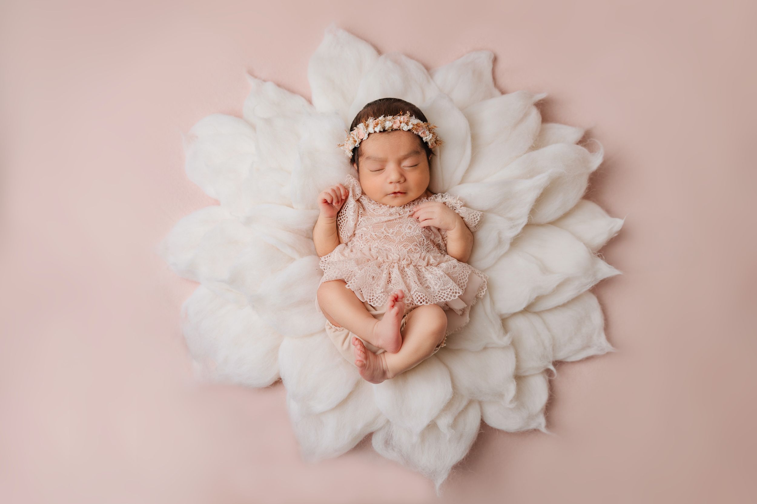 Sleeping newborn on white flower-shaped backdrop wearing delicate pink outfit.