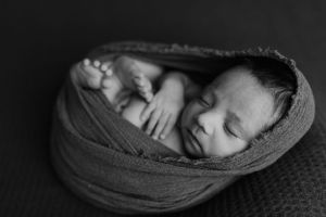 Sleeping baby wrapped in gray fabric in artistic black and white portrait.