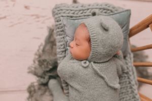 Newborn baby wearing soft gray knit bonnet sleeping on textured blanket.