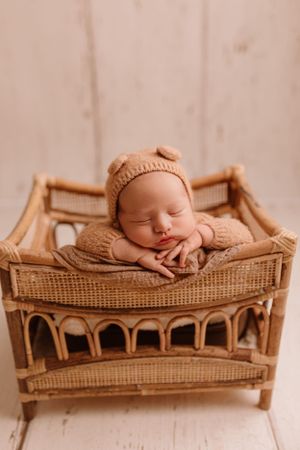 Sleeping baby in cozy knit outfit resting in decorative rattan bassinet.