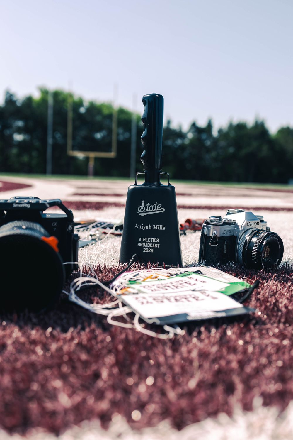 Mills athletics broadcast award trophy displayed on track field with vintage cameras and press credentials.