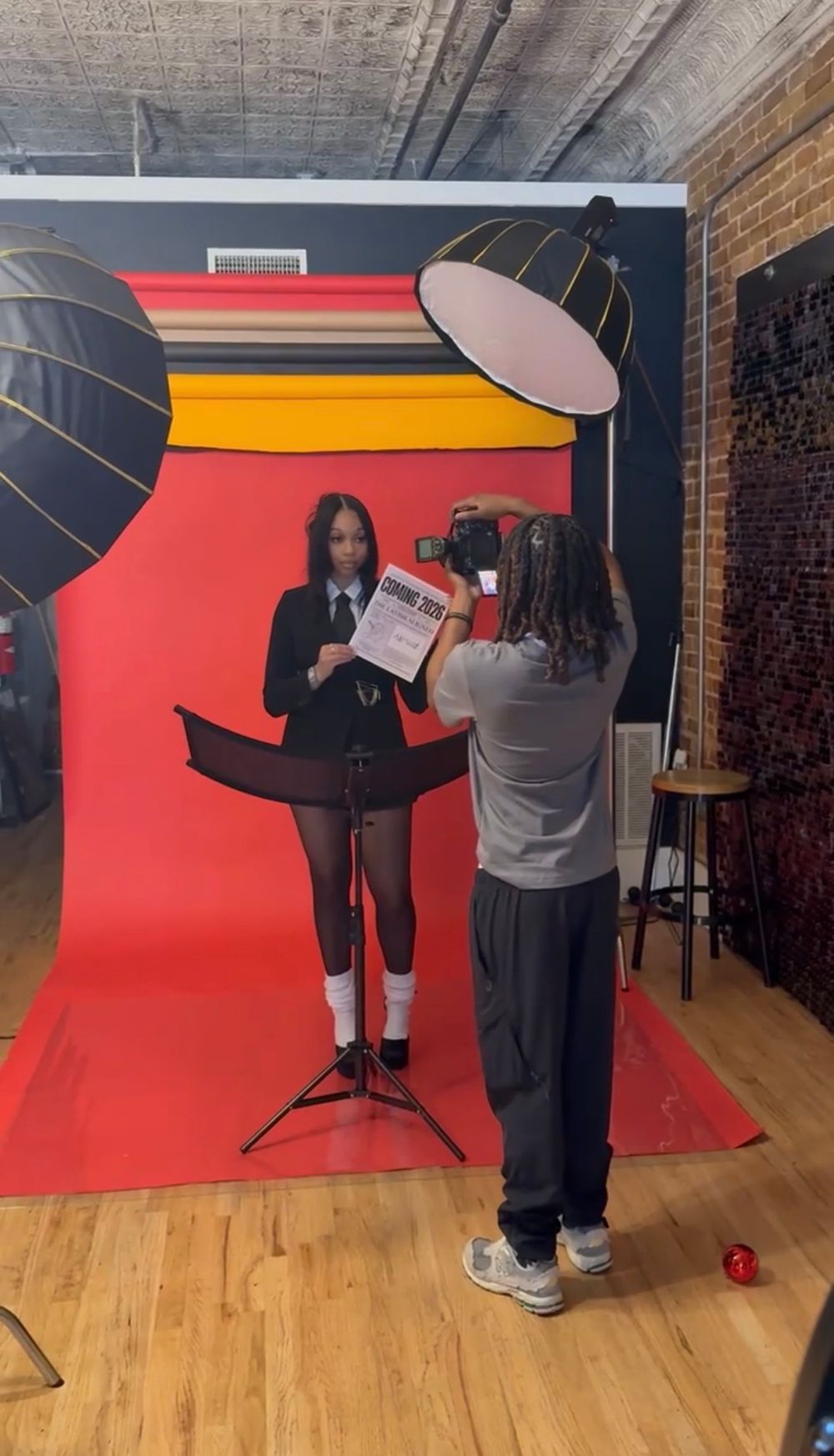 Mills shooting model holding newspaper in front of red backdrop in professional studio.