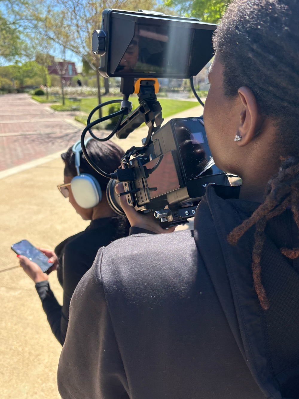 Mills filming outdoors with a professional camera rig on a sunny day on a brick plaza.
