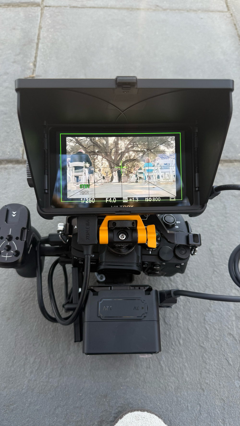 Professional cinema camera rig with external monitor displaying live street scene footage on a concrete surface.