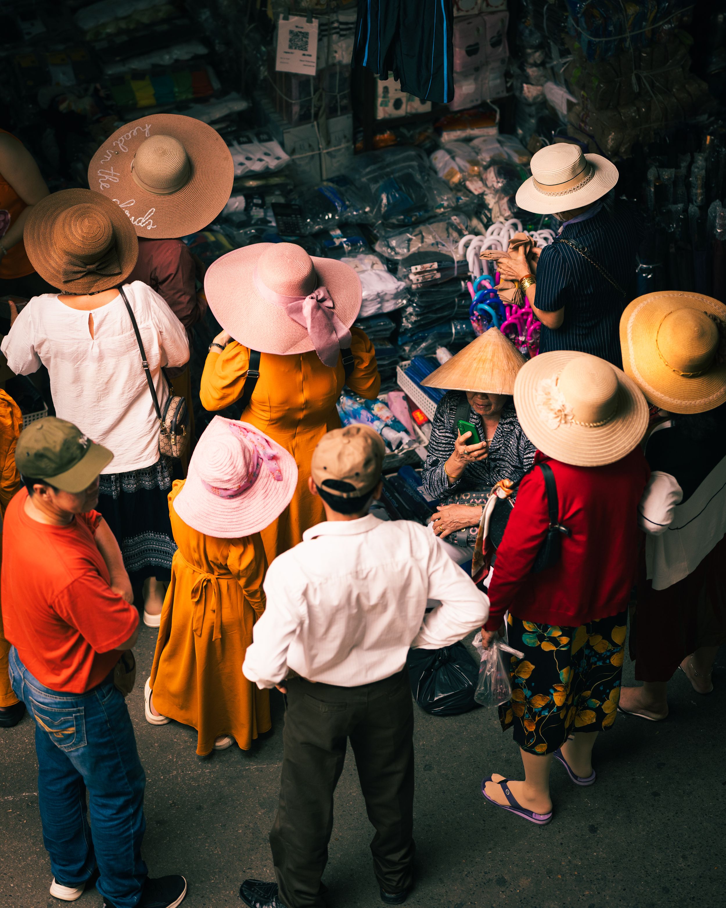 Group of people wearing straw hats gathered at outdoor market stall in Vietnam. Photograph by Chris Ha.