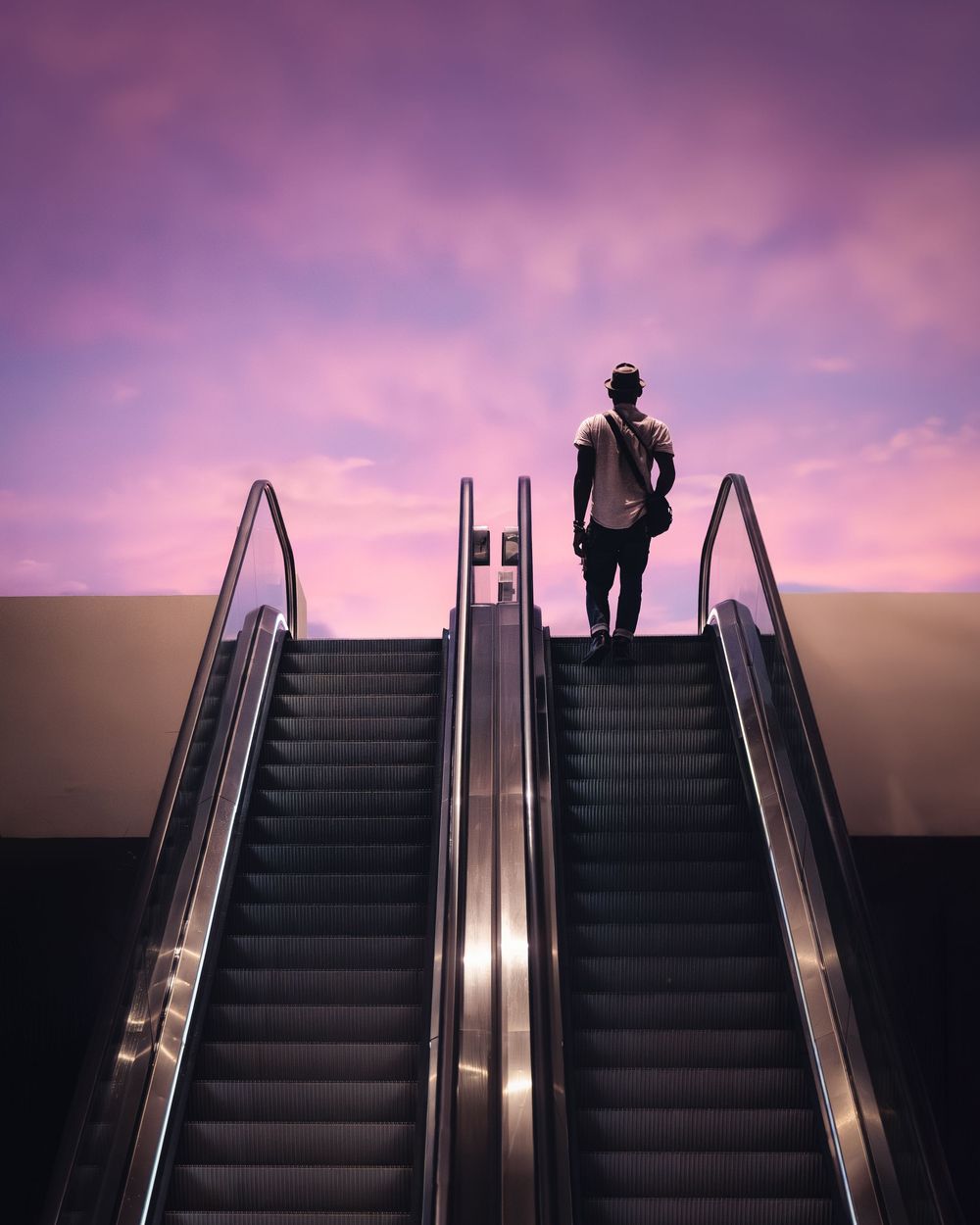 A silhouette stands atop an escalator against a vibrant purple sunset sky. Photograph by Chris Ha.
