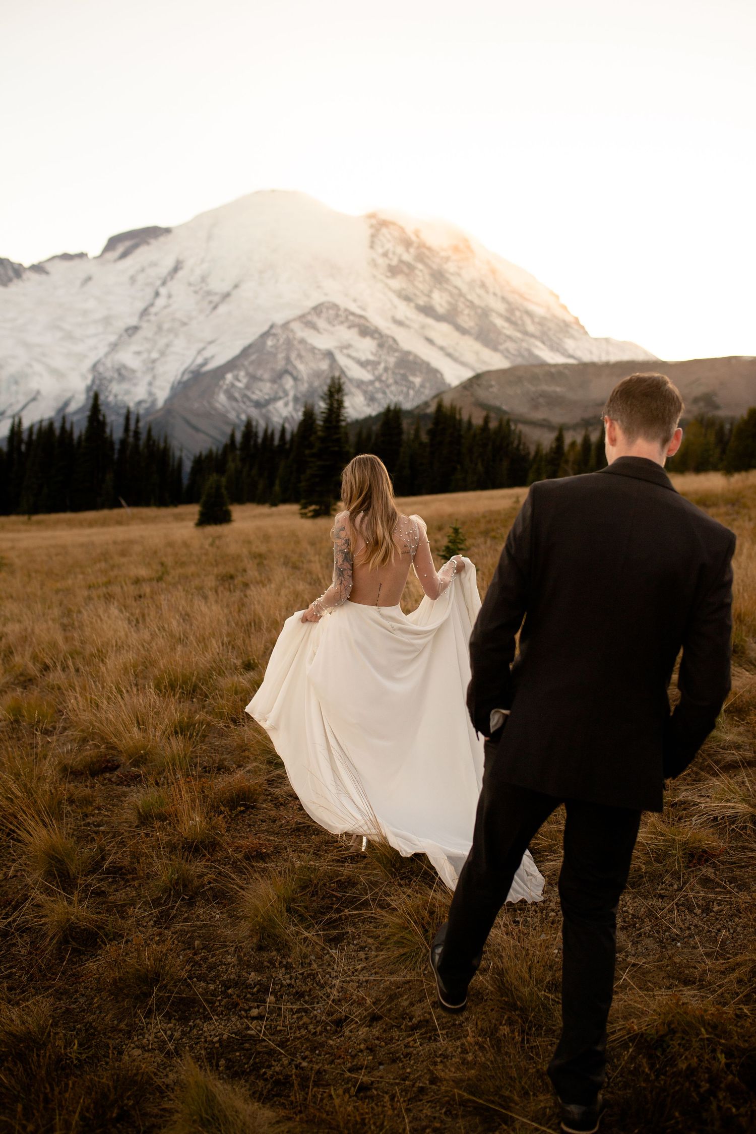 Husband and wife walking through a mountainside field at golden hour during their Mount Rainier elopement