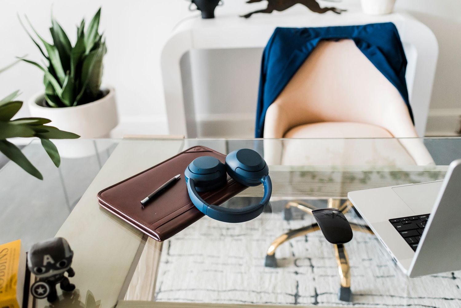A desk surface displays a laptop, planner, sunglasses, and keys with a small potted plant in the background.