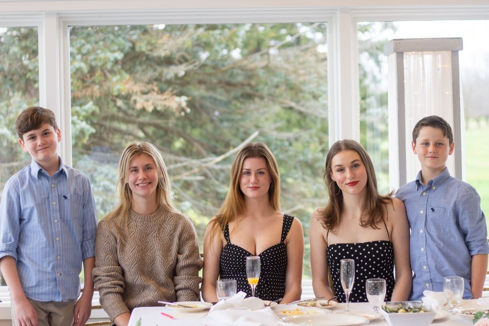 A large group sits together at a long dining table on an outdoor patio at an engagement party for family photos.