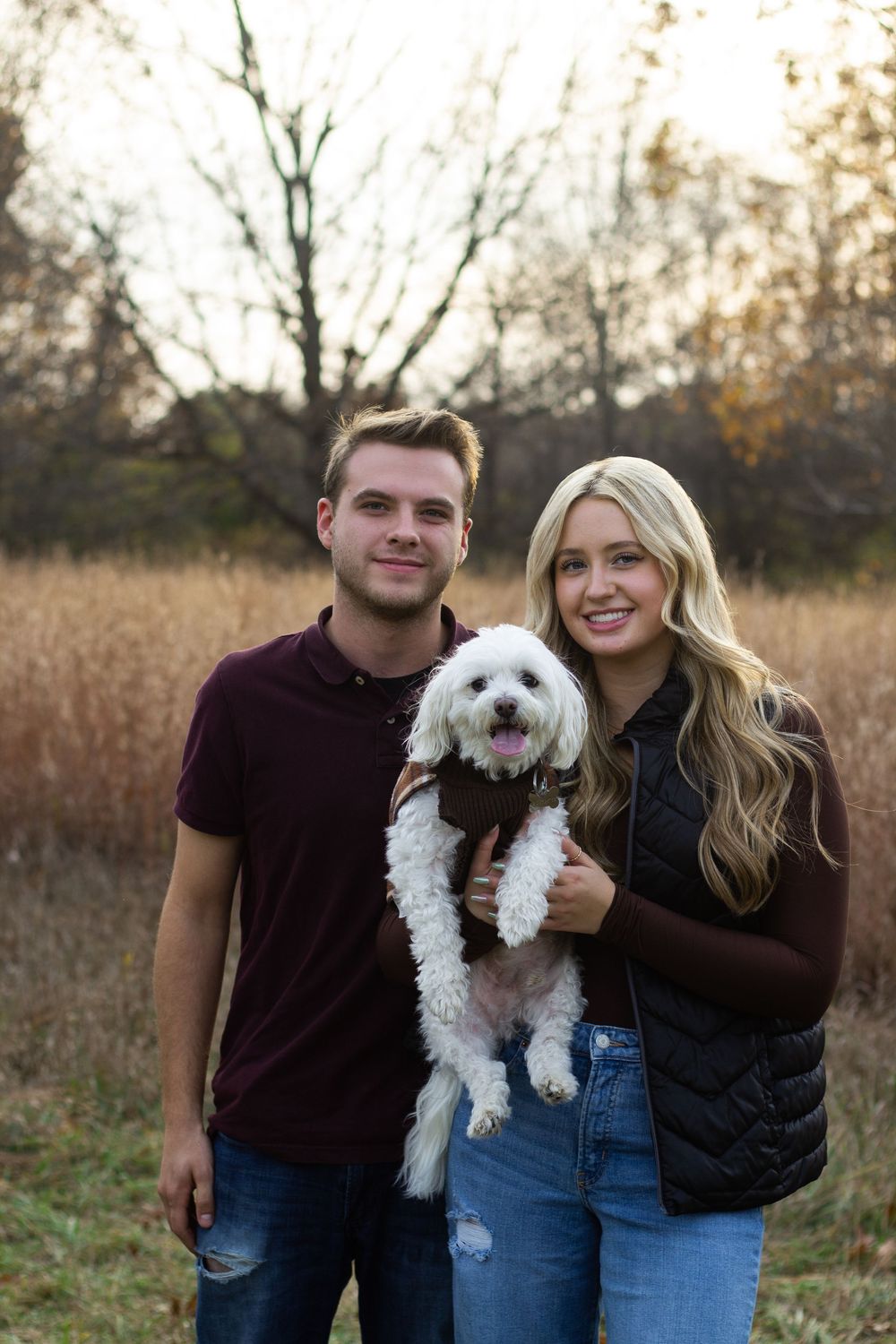 A group of people and a white fluffy dog pose together in a rustic outdoor setting during golden hour for family portraits.