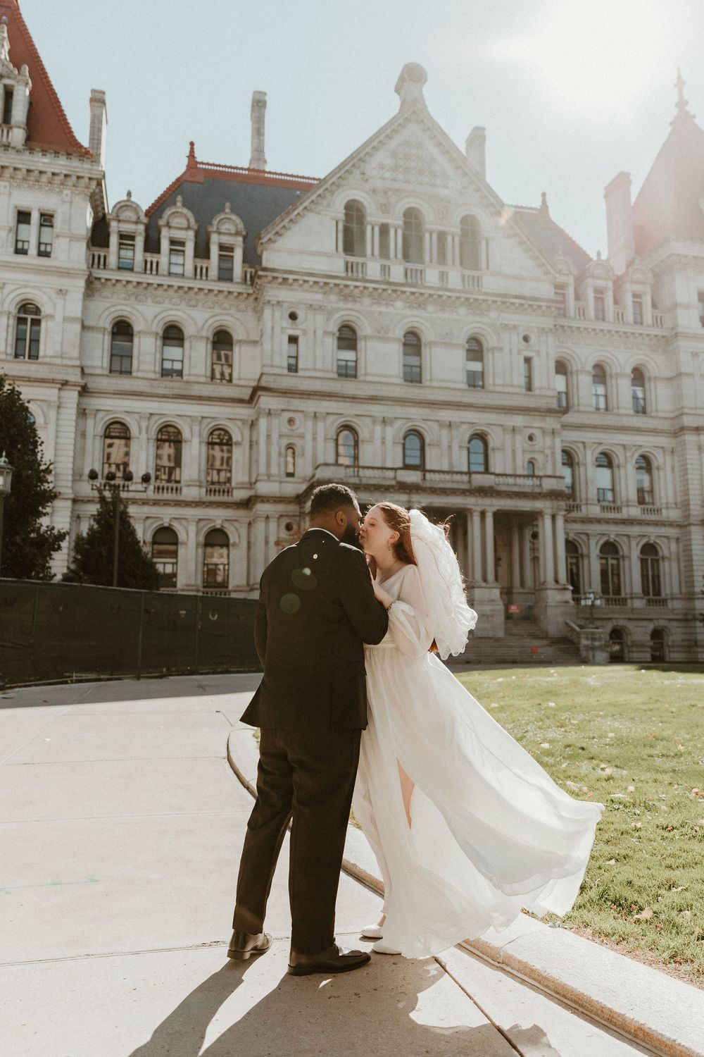 Wedding couple dances in front of a grand historic building with ornate architecture.