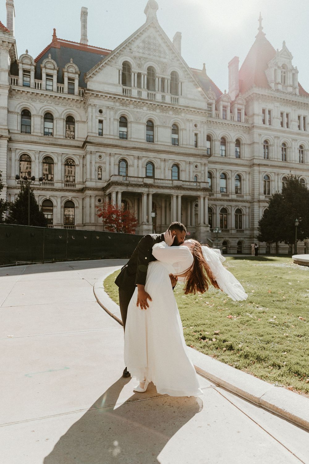 Newlyweds dance and twirl in front of a majestic Victorian-style building.
