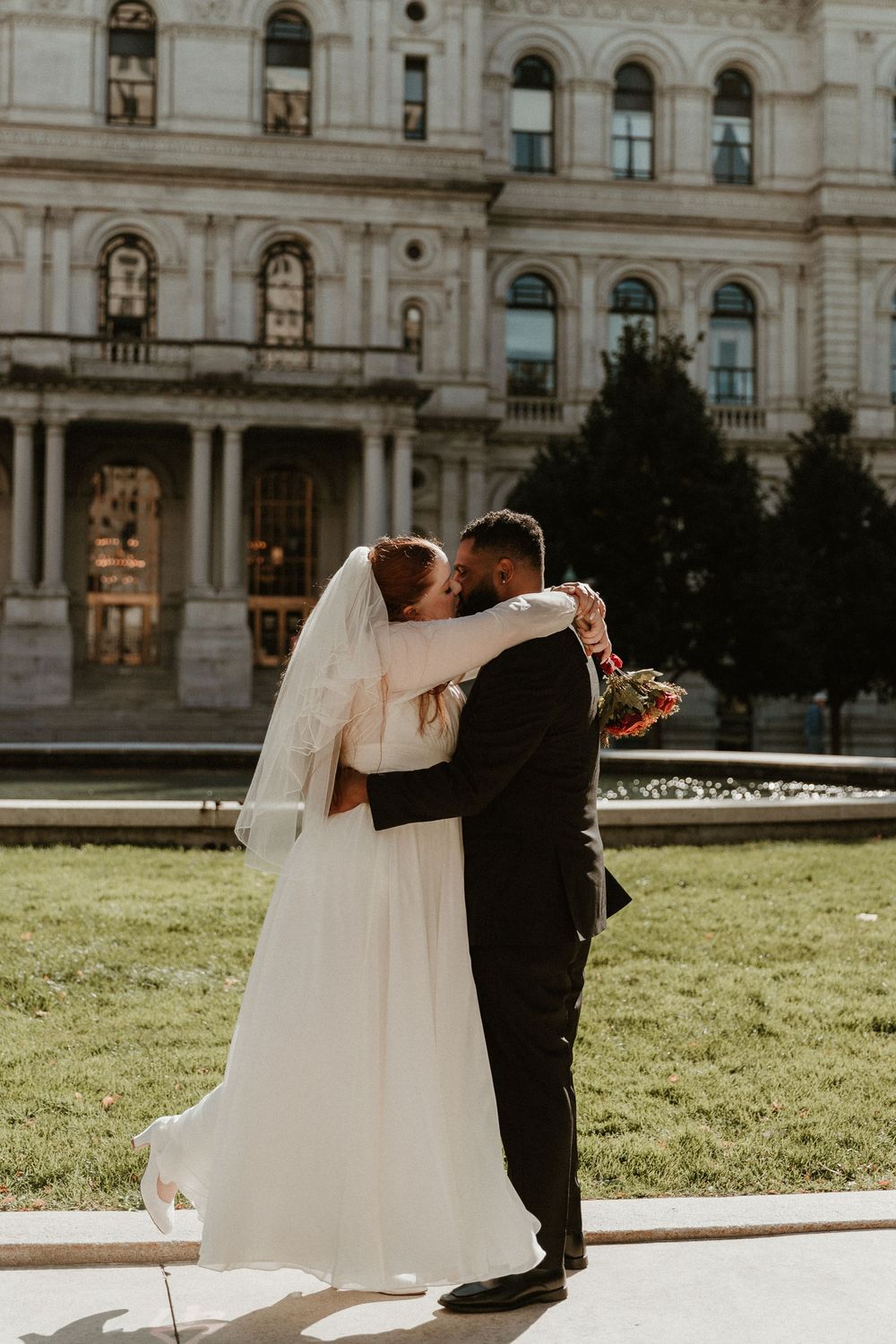 A bride and groom share their first dance on their wedding day in front of a historic building.