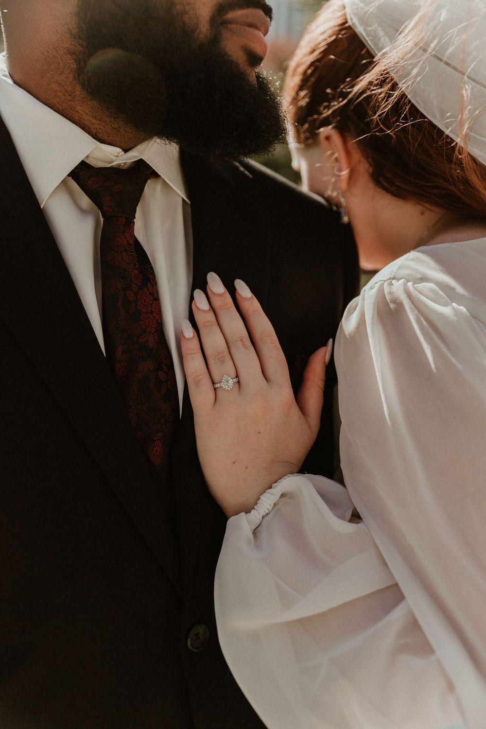 Close-up shot of a bride's hand with engagement ring resting on groom's formal suit.