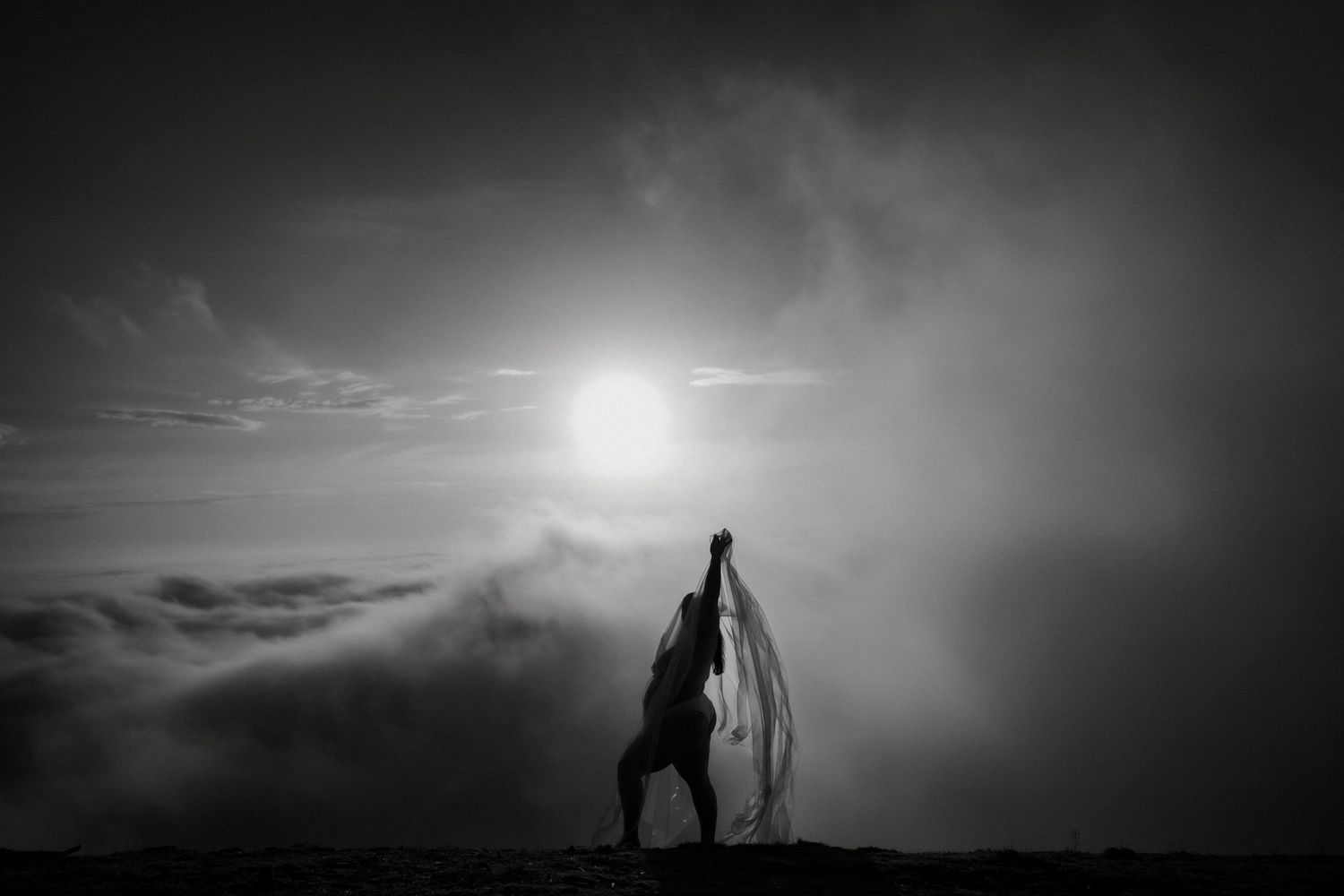 A dramatic black and white silhouette against cloudy sunset sky with billowing fabric.
