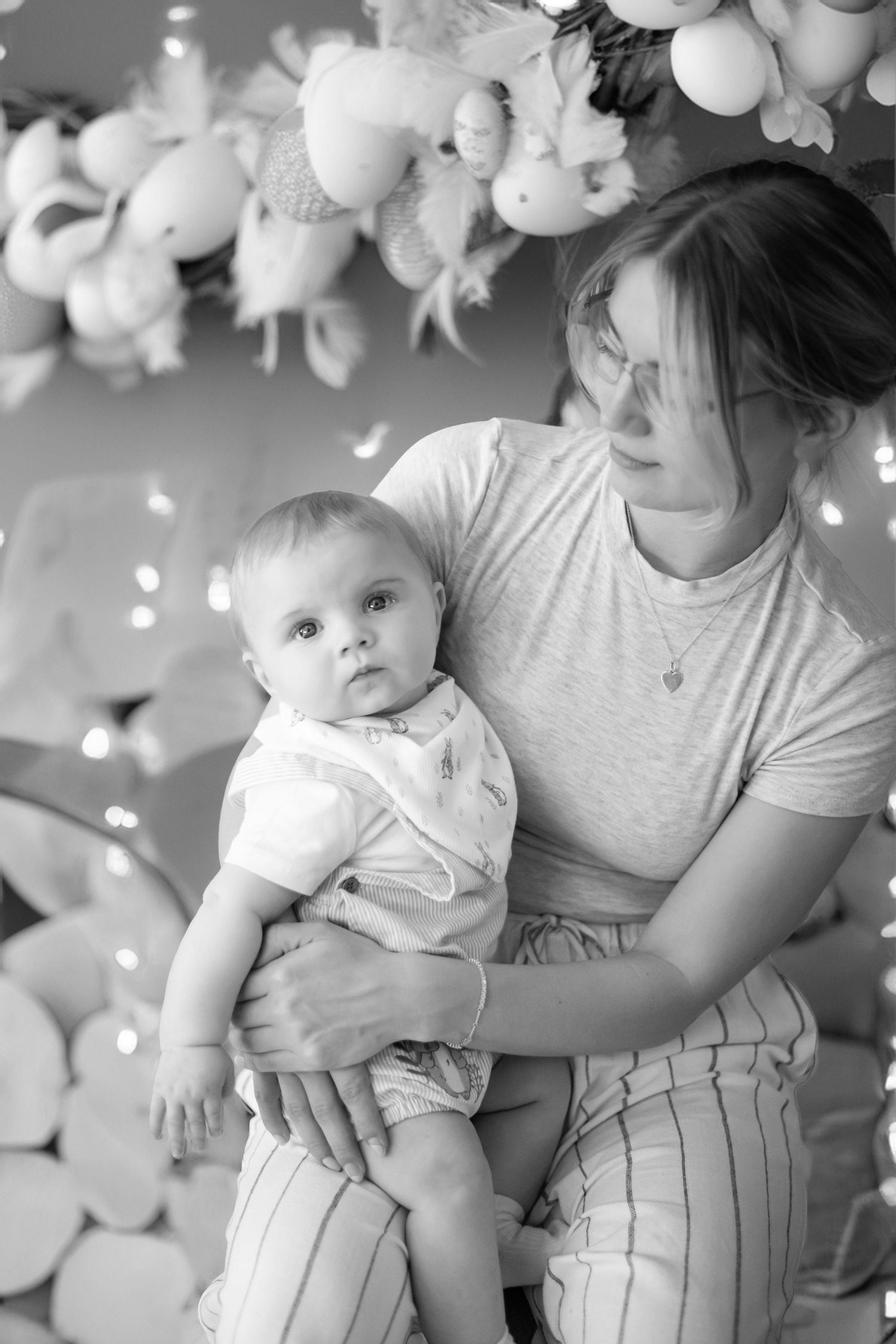 Black and white photo of a baby being held against a backdrop with stuffed animals and twinkle lights.