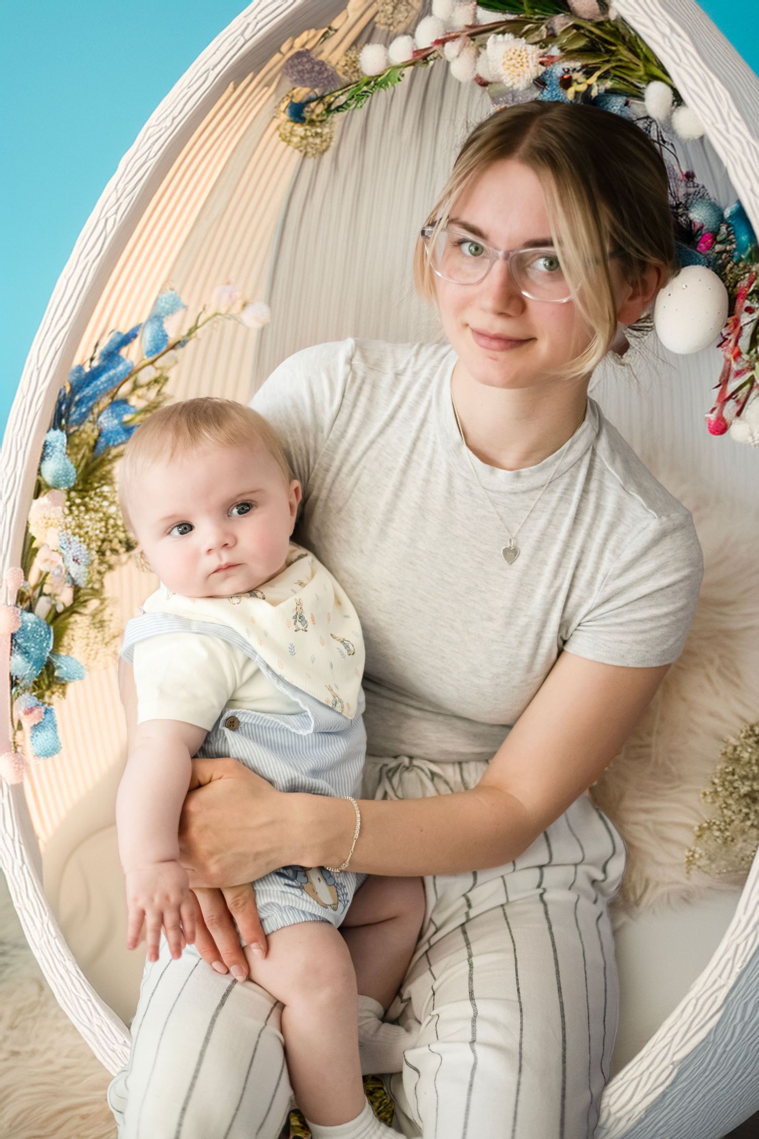 Sweet portrait with a baby and caregiver sitting in a white oval chair surrounded by blue and white floral decorations.