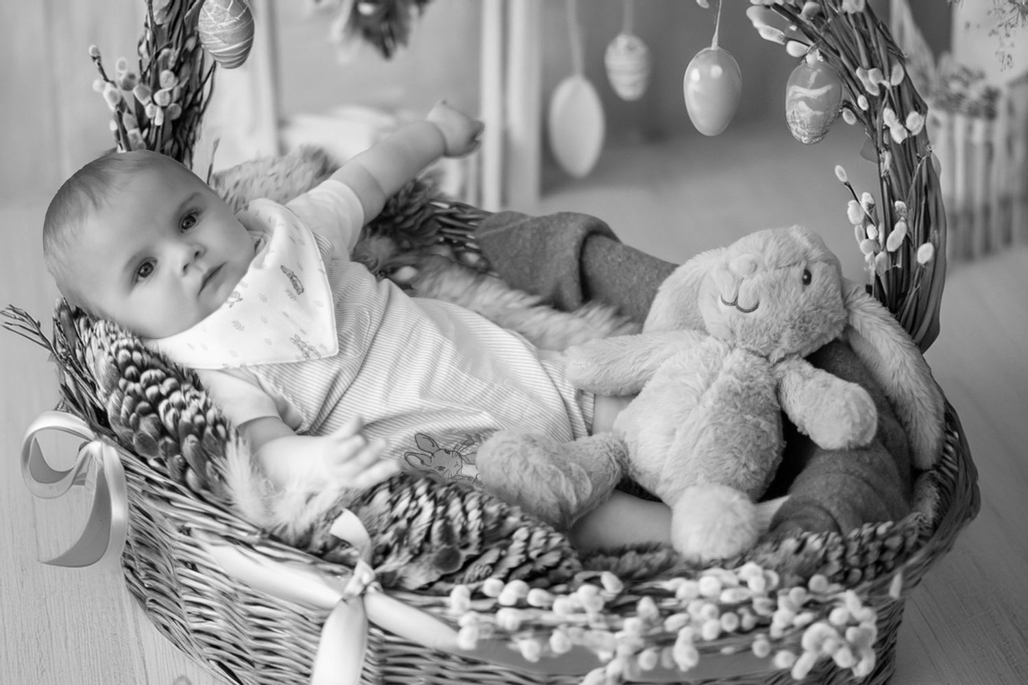 Black and white photo of a baby resting in a wicker basket with a plush toy bunny beside them.